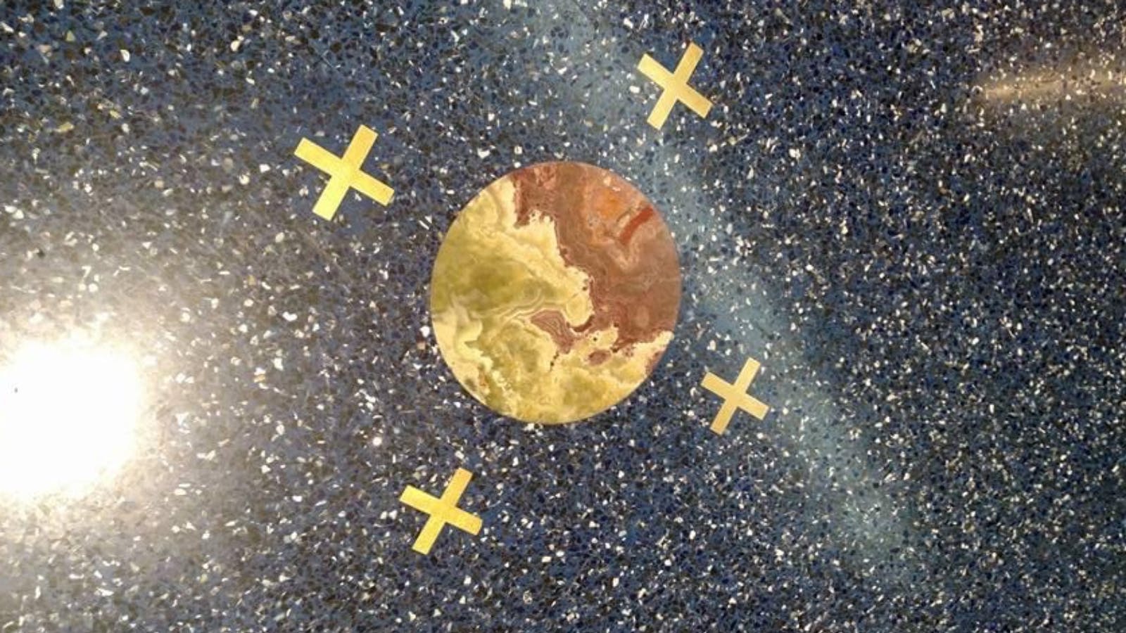 Circular mosaic on a blue speckled floor at Kansas City International Airport, surrounded by four gold X shapes.