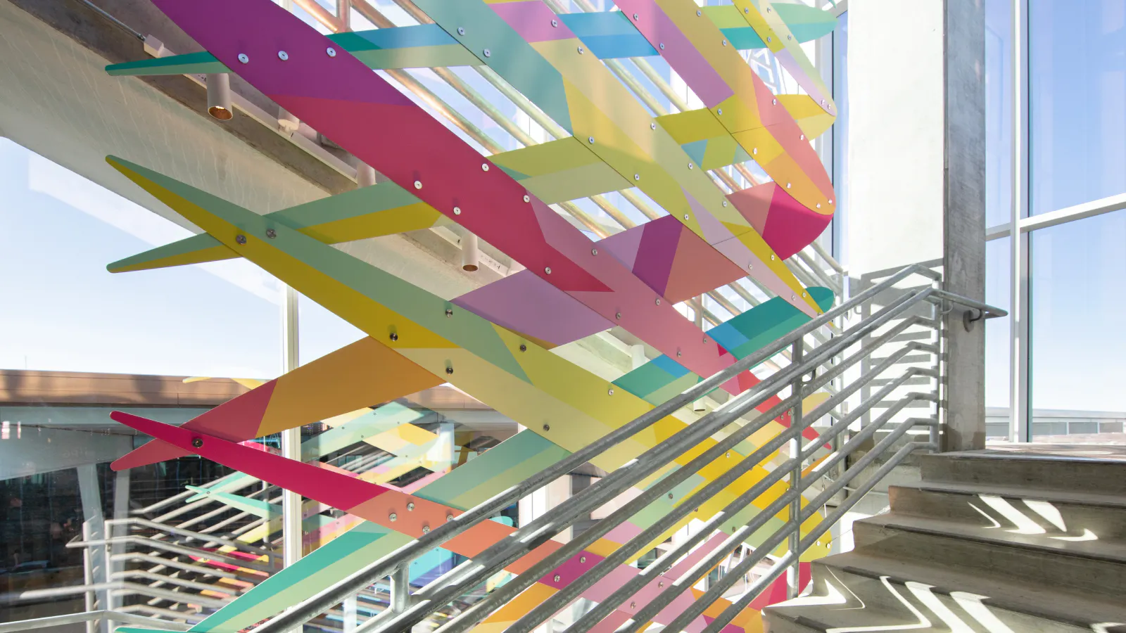 Interior view of a stairwell at Kansas City International Airport's parking garage with a colorful layered sculpture made of overlapping diagonal panels in pink, yellow, green, and blue.