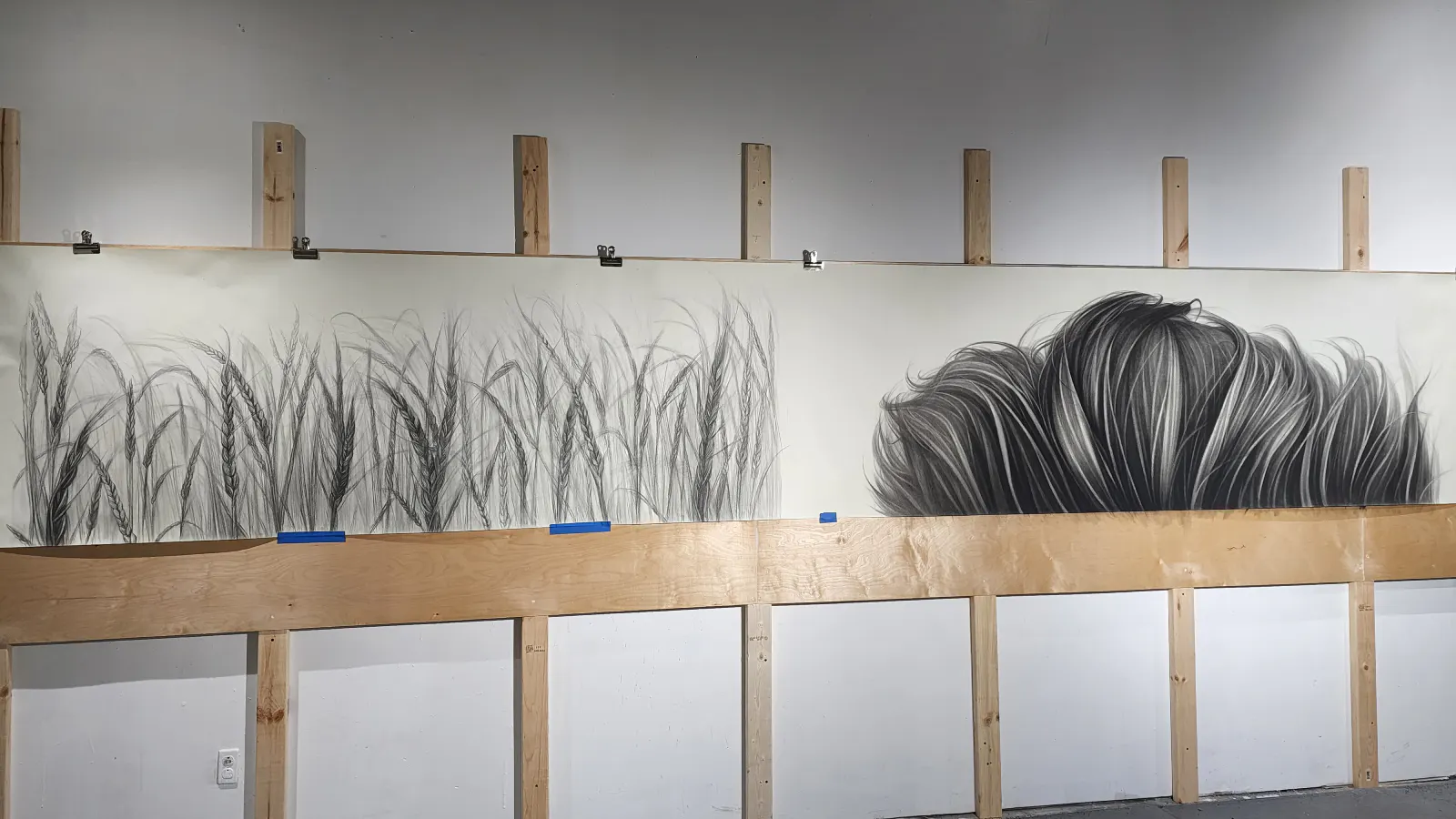 Unframed panoramic artwork in progress, featuring a transition from detailed wheat stalks on the left to sweeping, wind-blown grass forms on the right, pinned to a wooden support wall.