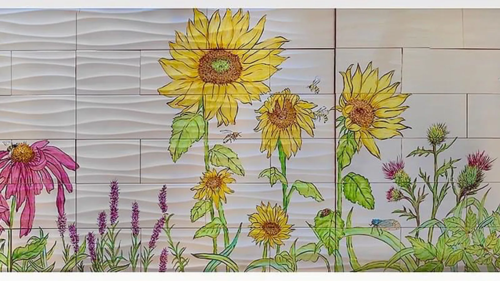 Close-up of sunflowers, thistles, and bees in a vibrant tile mural, with textured white background tiles that resemble gentle waves.