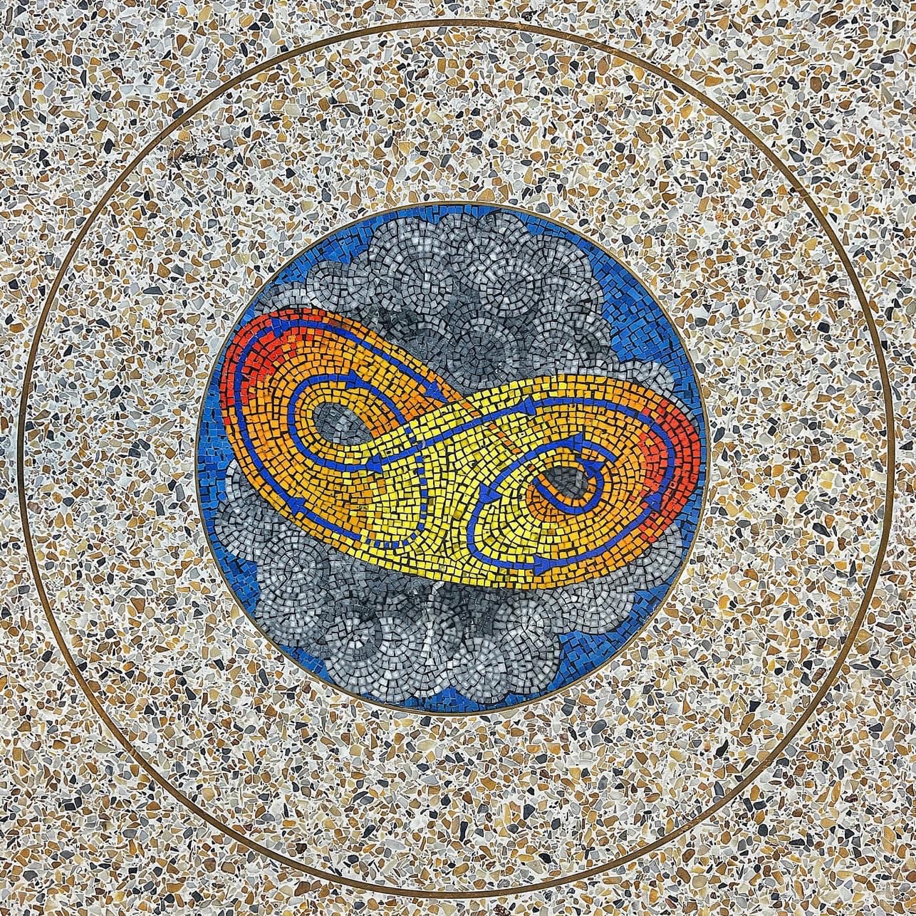 Circular mosaic in a terrazzo floor showing a swirling yellow and red infinity shape against a background of gray clouds and blue sky.