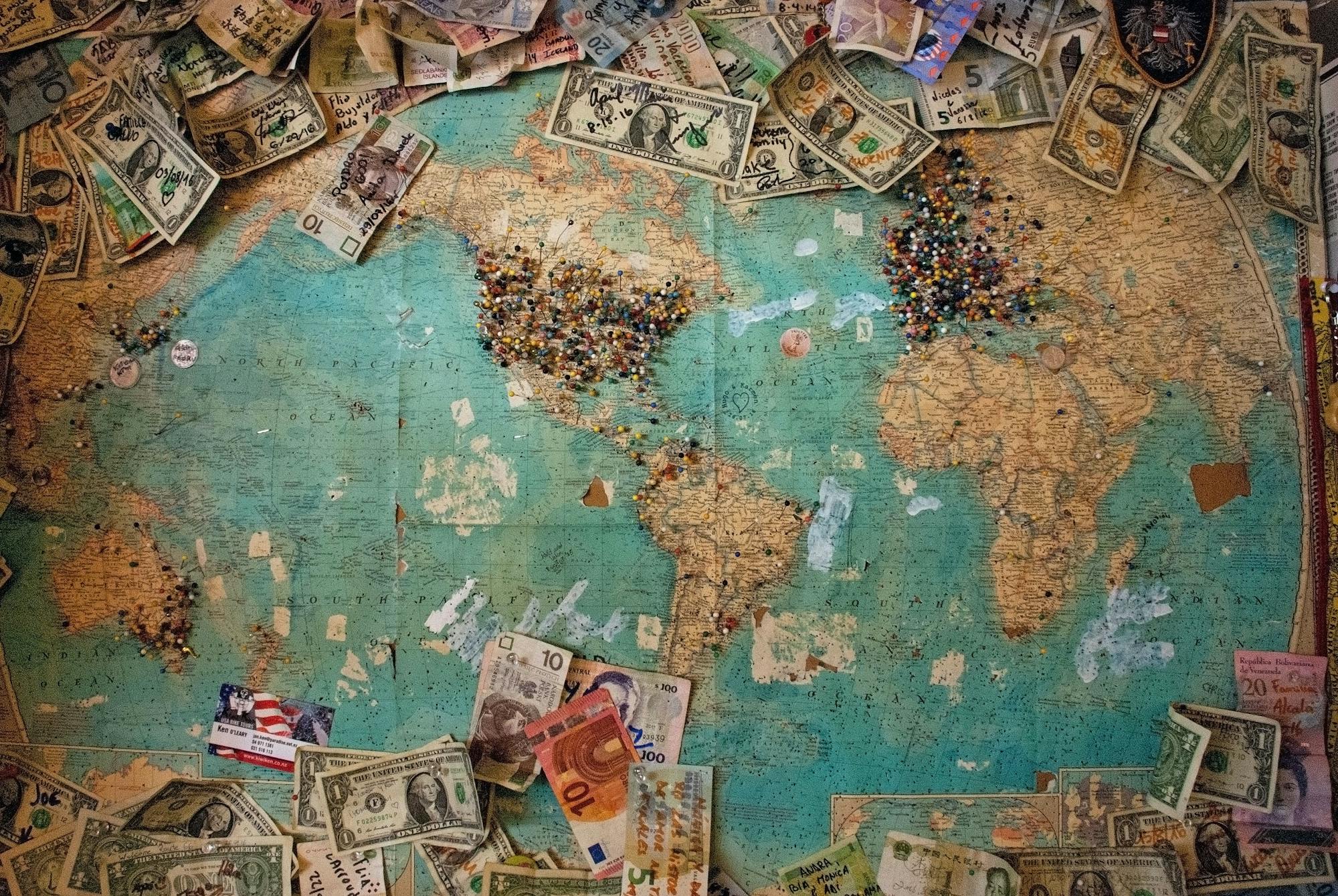 Weltkarte, auf der sich zahlreiche Geldscheine aus unterschiedlichen Ländern befinden