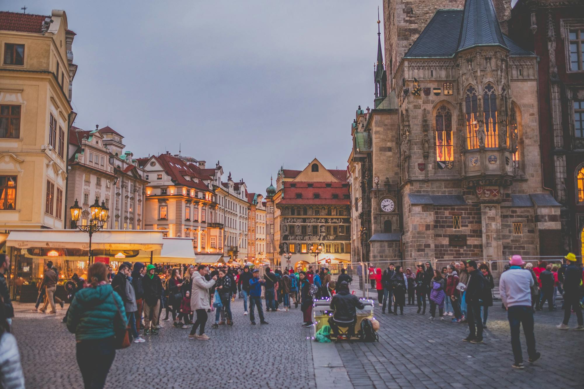Innenstadt von Prag mit dem Prager Rathaus, Straßenmusikern und zahlreichen Besucher:innen.