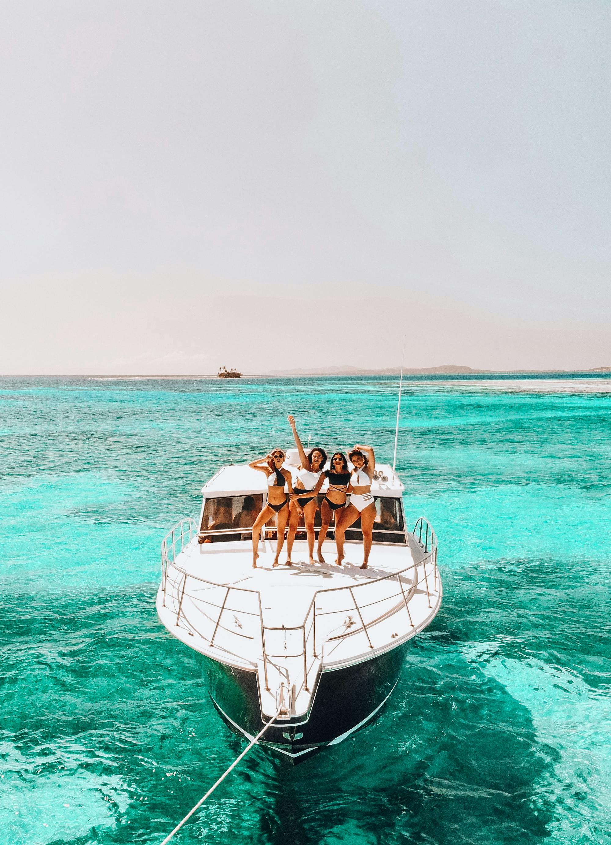 Vier Frauen tanzen auf dem Deck eines Bootes. Um sie herum ist einzig und allein strahlend blaues Meer. 