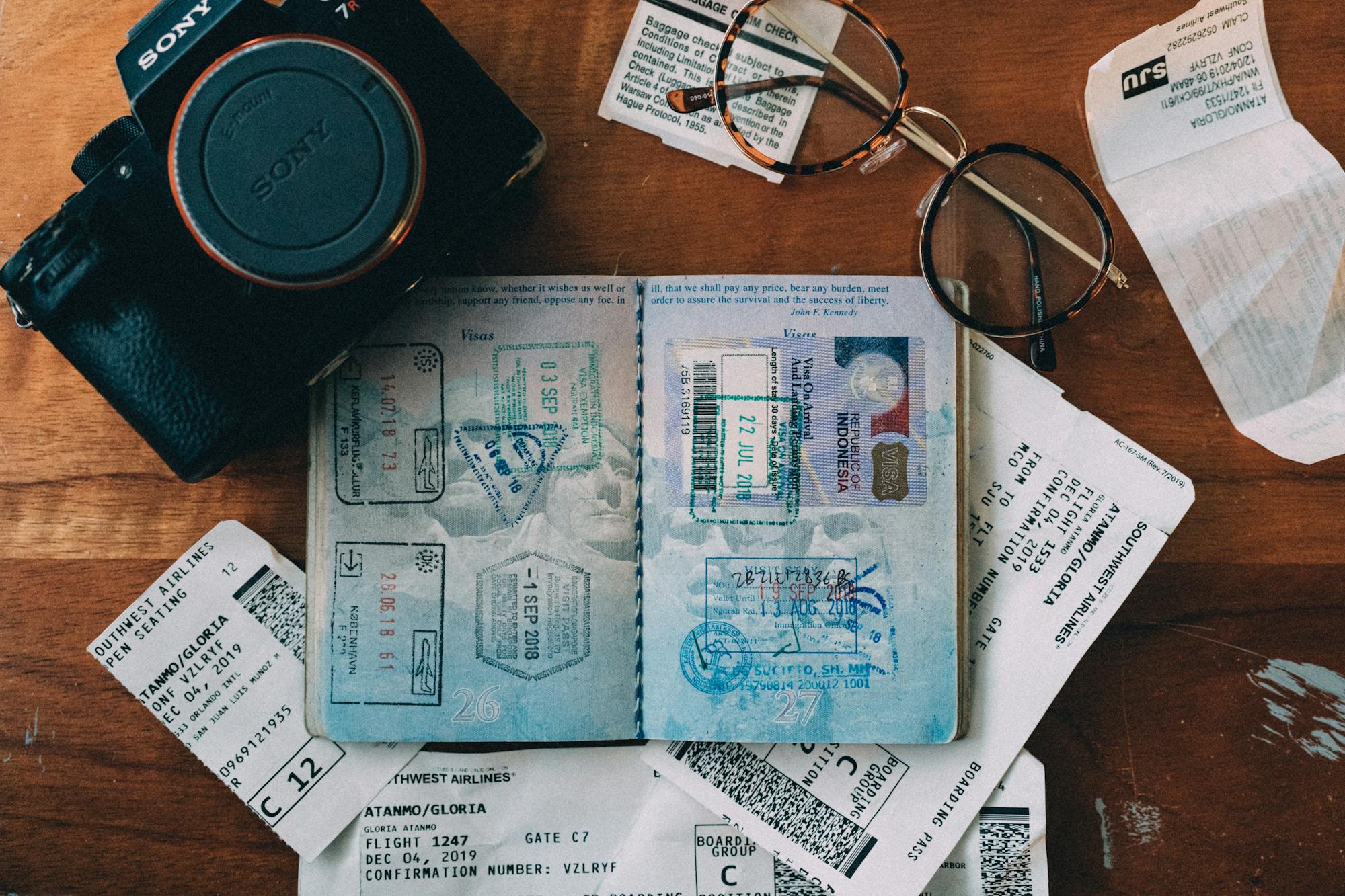 Auf dem Schreibtisch liegen alle essentiellen "Reisebegleiter": Kamera, Reisepass, Brille und das Flugticket. 