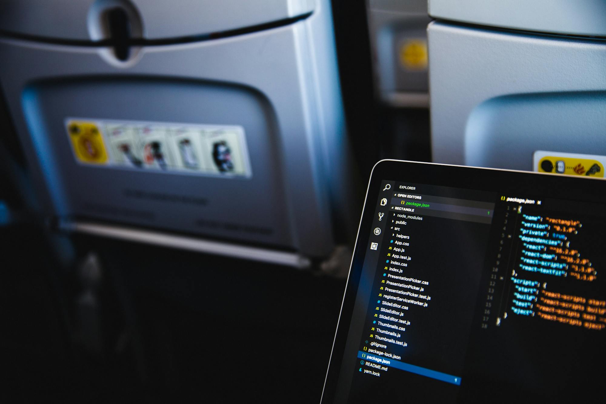 Otwarty laptop na kolanach pasażera samolotu. Na ekranie widoczne są różne kody programistyczne/matematyczne.