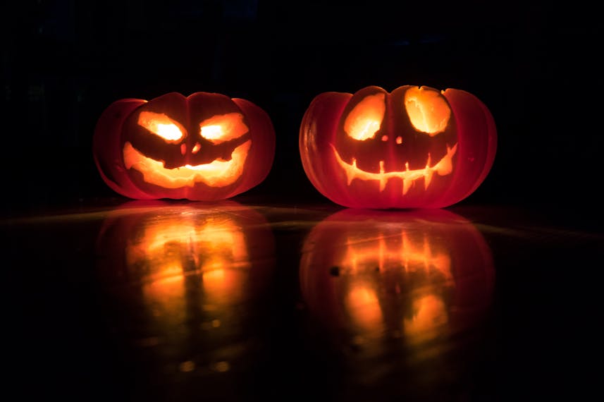 Dwa wydrążone dynie na Halloween świecą w ciemności. Płonące świeczki w środku dyni odsłaniają wyrzeźbione twarze.