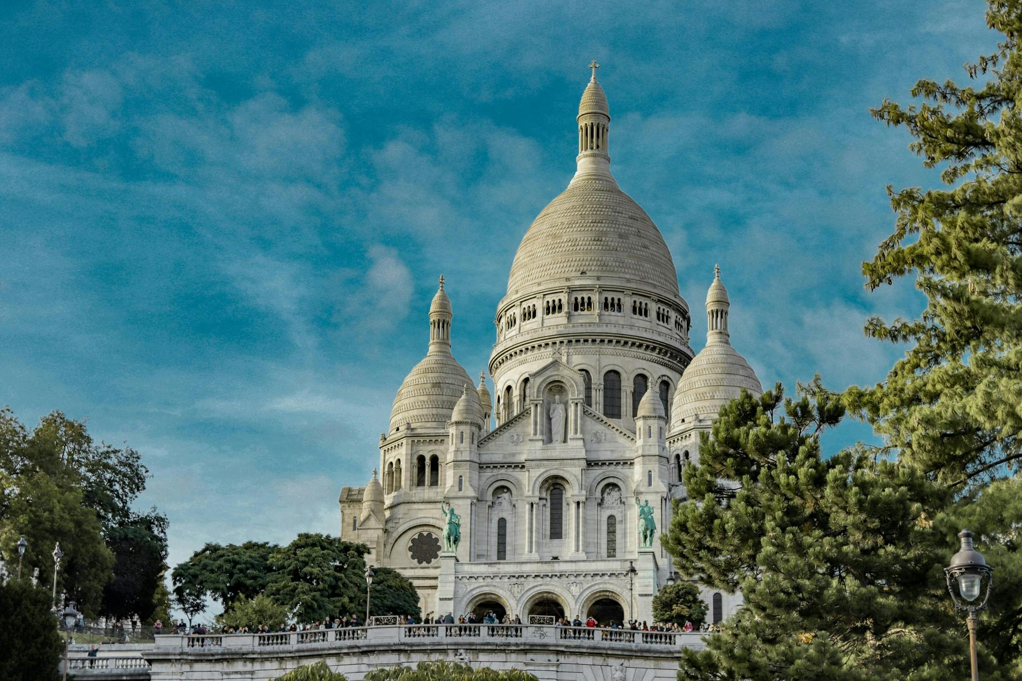 Low angle exterior of famous Sacre Coeur Basilica with domes and arched windows located on Montmartre hill in Paris against blue sky