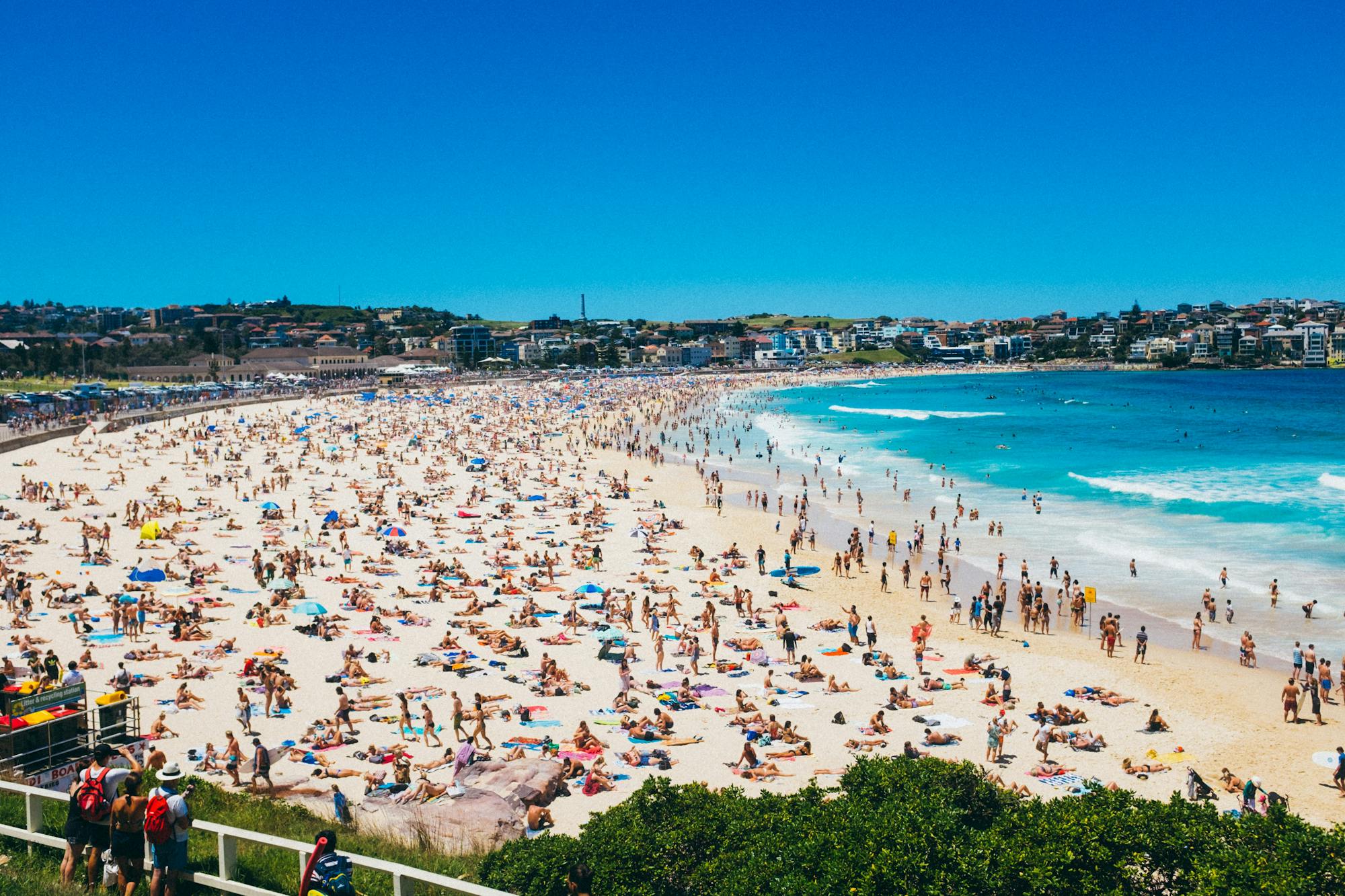 Widok na plażę Bondi z tysiącami ludzi leżących na plaży i kąpiących się w morzu.