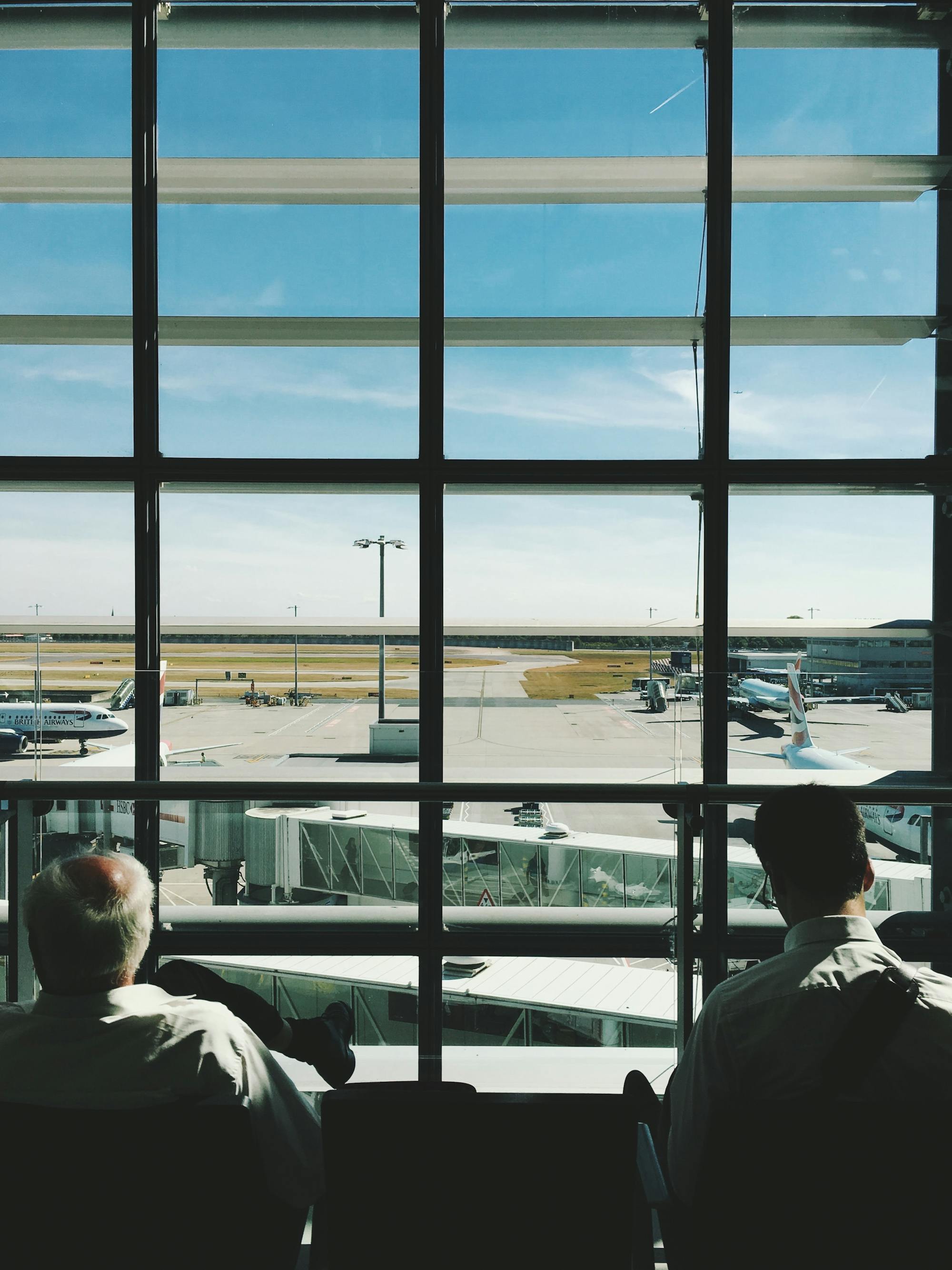 Zwei Personen sitzen am Fluggate und blicken aus dem Fenster. Sie sehen dem Flugbetrieb zu. 
