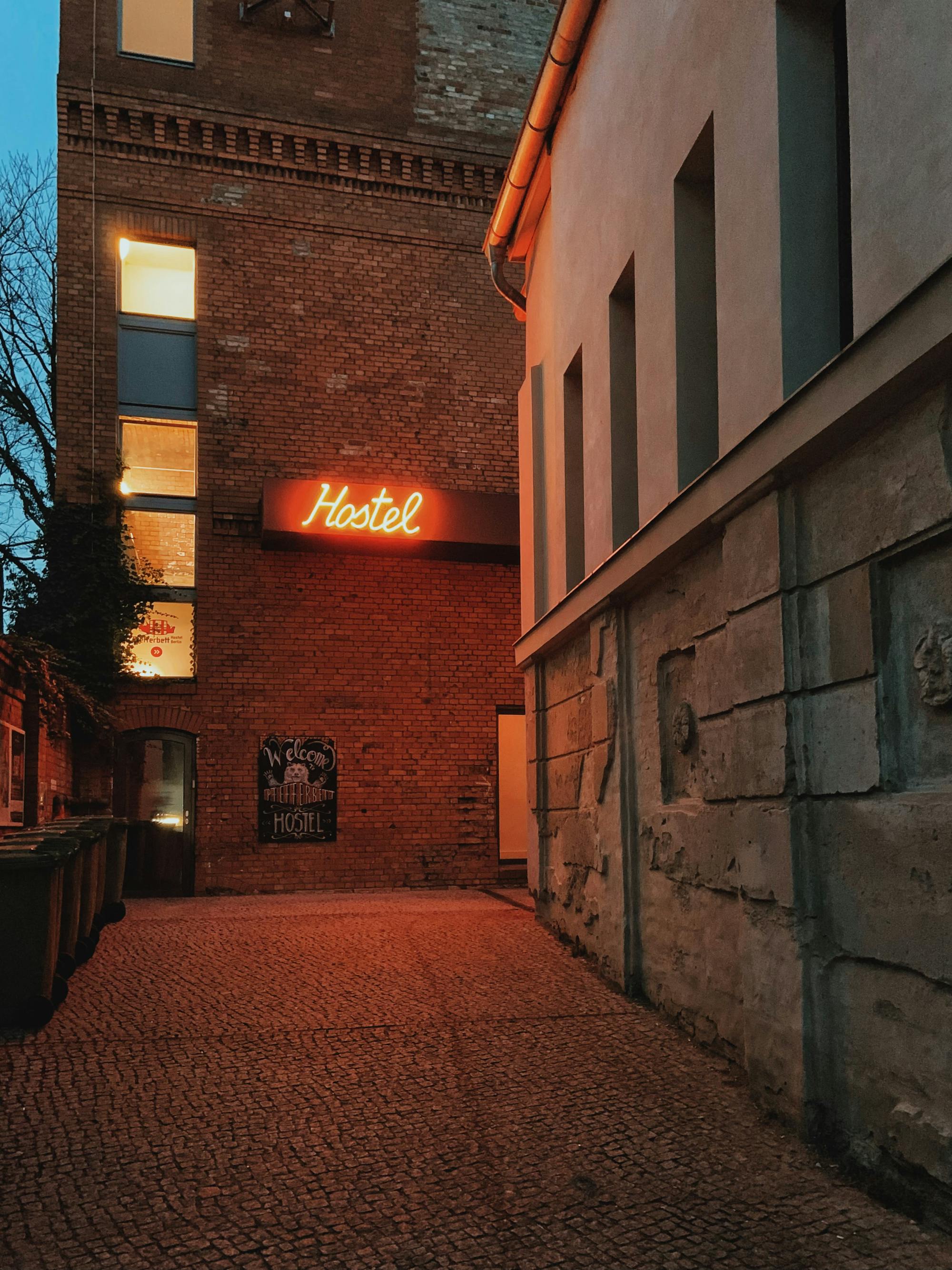 In der Hintergasse befindet sich an der Hausfassade eines alten Gebäudes ein roter, neonfarbiger Schriftzug mit der Aufschrift "Hostel"