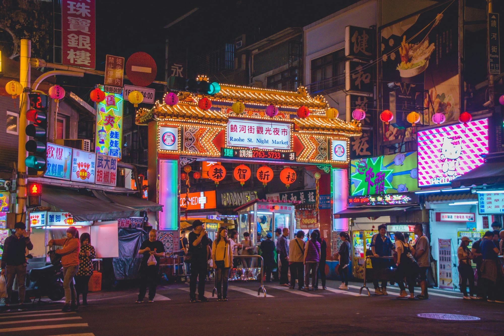 Die Menschen schlendern durch den Nachtmarkt. Viele bunte Werbelichter erhellen die Straßen in Taipei.  