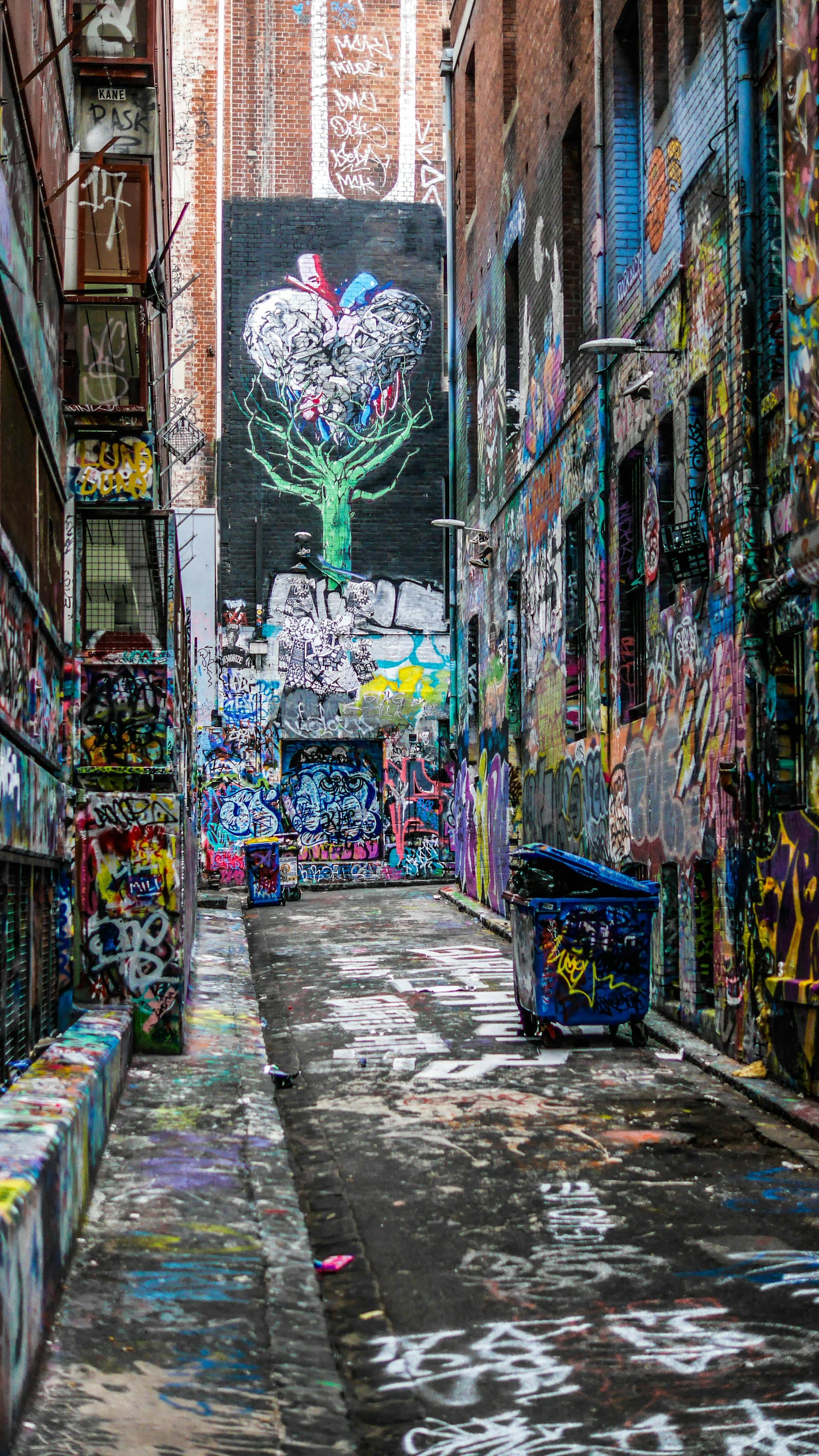 Boczna uliczka całkowicie pokryta graffiti. Zarówno ściany domów, kontenery na śmieci, jak i ulice.