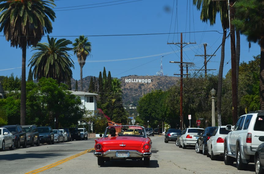Ein Cabrio fährt auf einer Straße in L.A. auf das Hollywood-Schild zu 