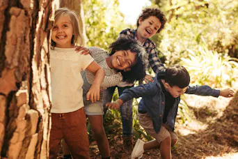 Vier Kinder spielen gemeinsam zwischen Bäumen in einem sonnigen Wald