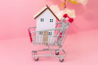 Kleines Modellhaus in einem Einkaufswagen vor rosa Hintergrund