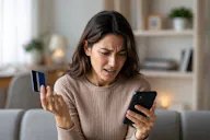 Frau hält eine Kreditkarte und blickt mit gerunzelter Stirn auf ihr Smartphone