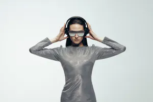 Modisches weibliches Model in einem silbernen Kleid, Sonnenbrille und Kopfhörer