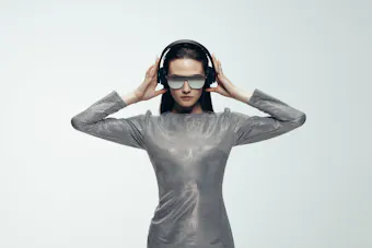 Modisches weibliches Model in einem silbernen Kleid, Sonnenbrille und Kopfhörer