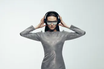 Modisches weibliches Model in einem silbernen Kleid, Sonnenbrille und Kopfhörer