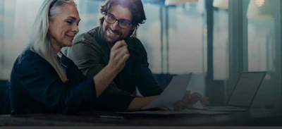 Geschäftsleute treffen sich im Büro und diskutieren über Dokumente. Geschäftsfrau mit einem Finanzbericht in der Hand sitzen mit männlichen Kollegen schauen sie und lächeln.