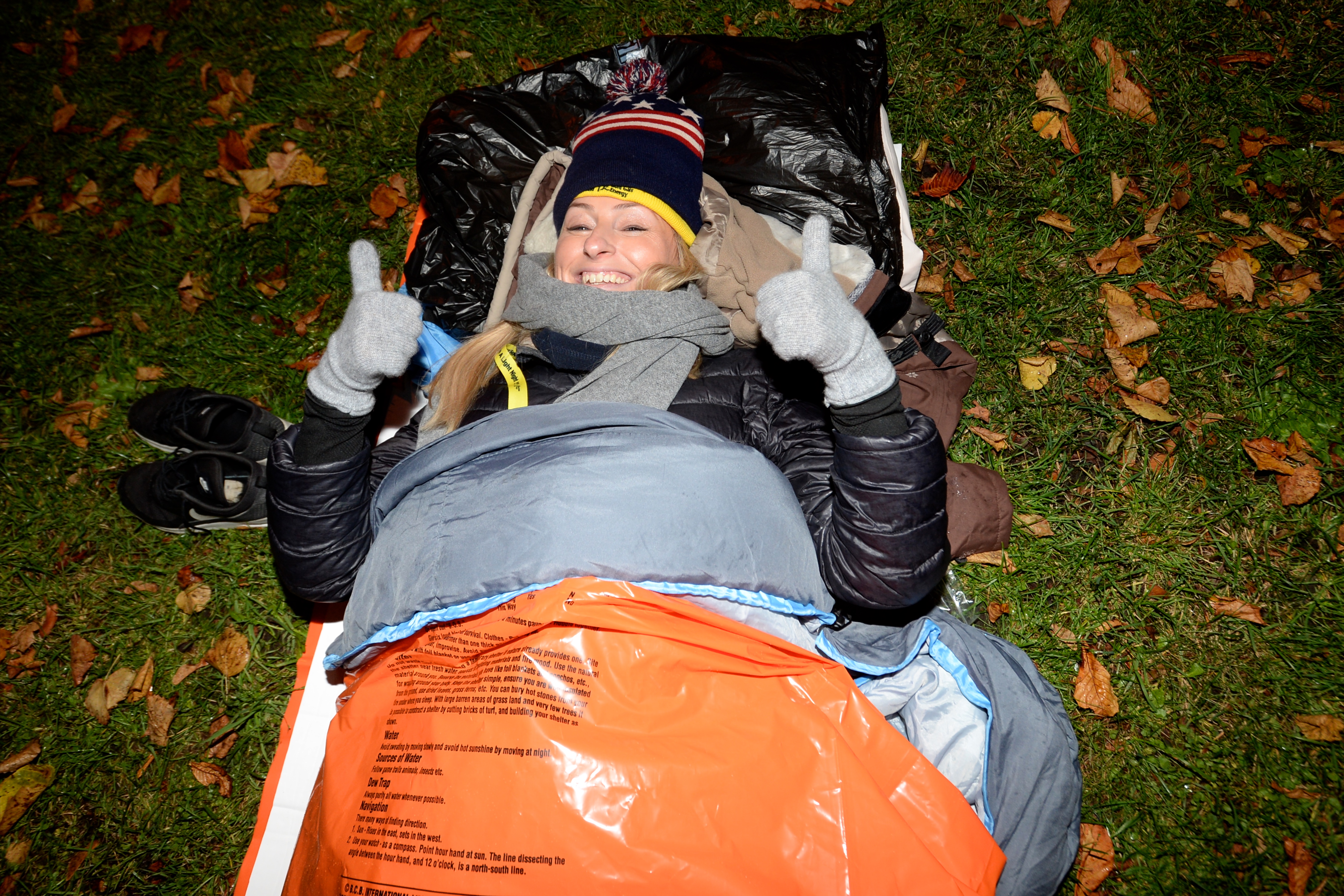 Woman in a sleeping bag outside smiling with her thumbs up to the camera