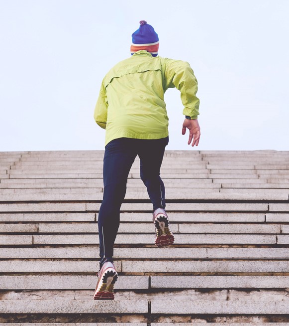 A person wearing a bright green raincoat and leggings running up a staircase - they have their back to the viewer so looking up at them ascending.