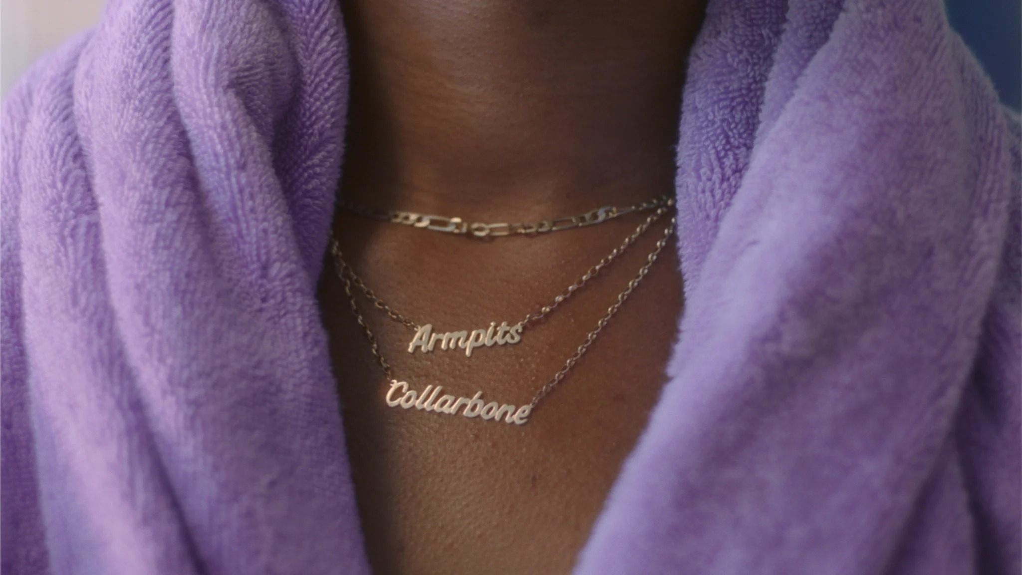 Woman with a purple towel around neck with a necklace that says: Armpits and Collarbone