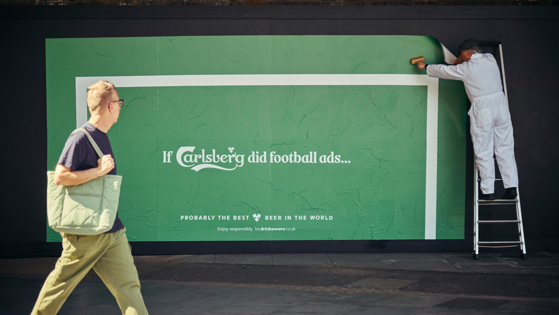 carlsberg poster on a street with a passerby and a man on the ladder