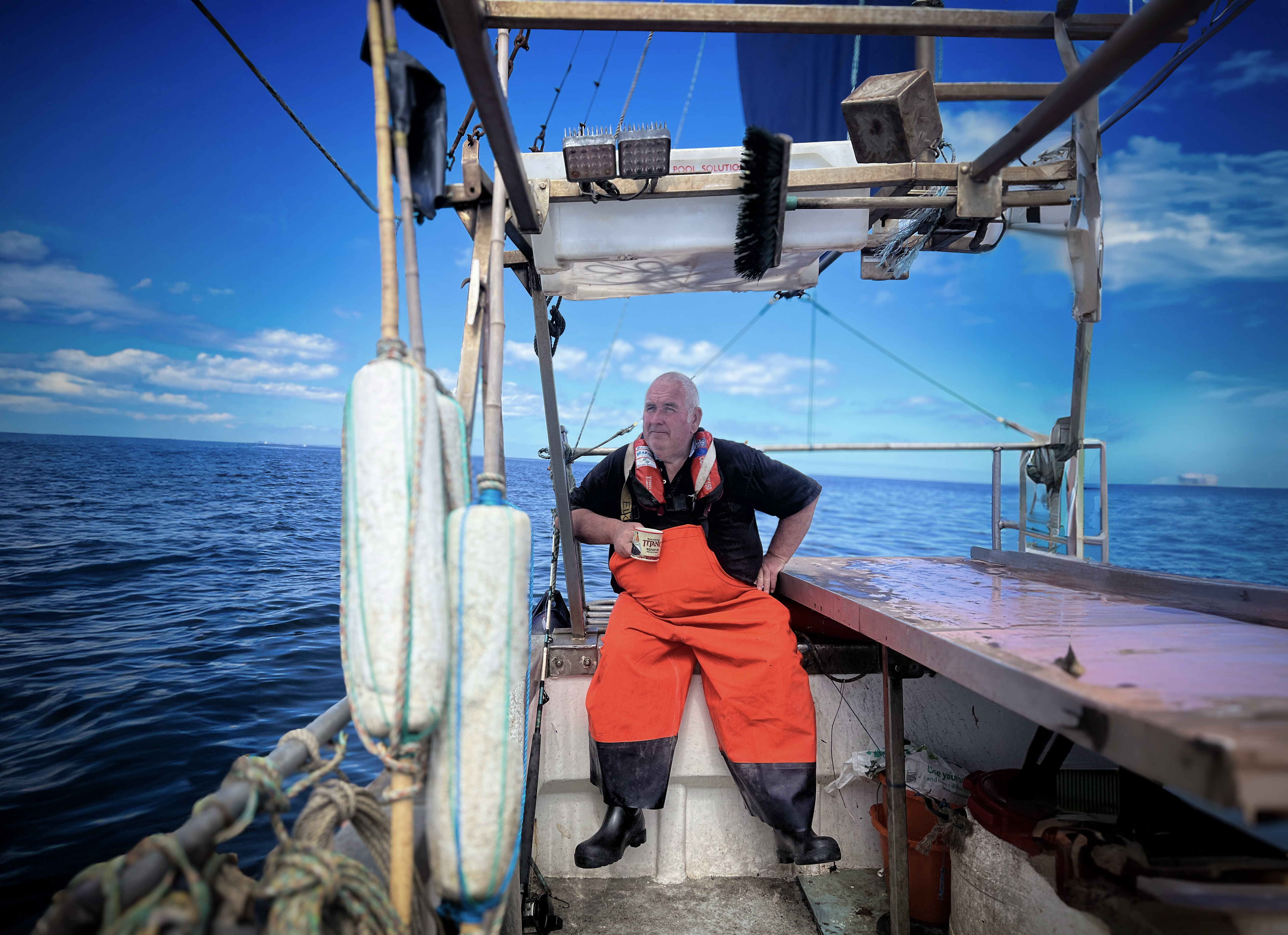 Fisherman in red overalls on a boat against blue sky