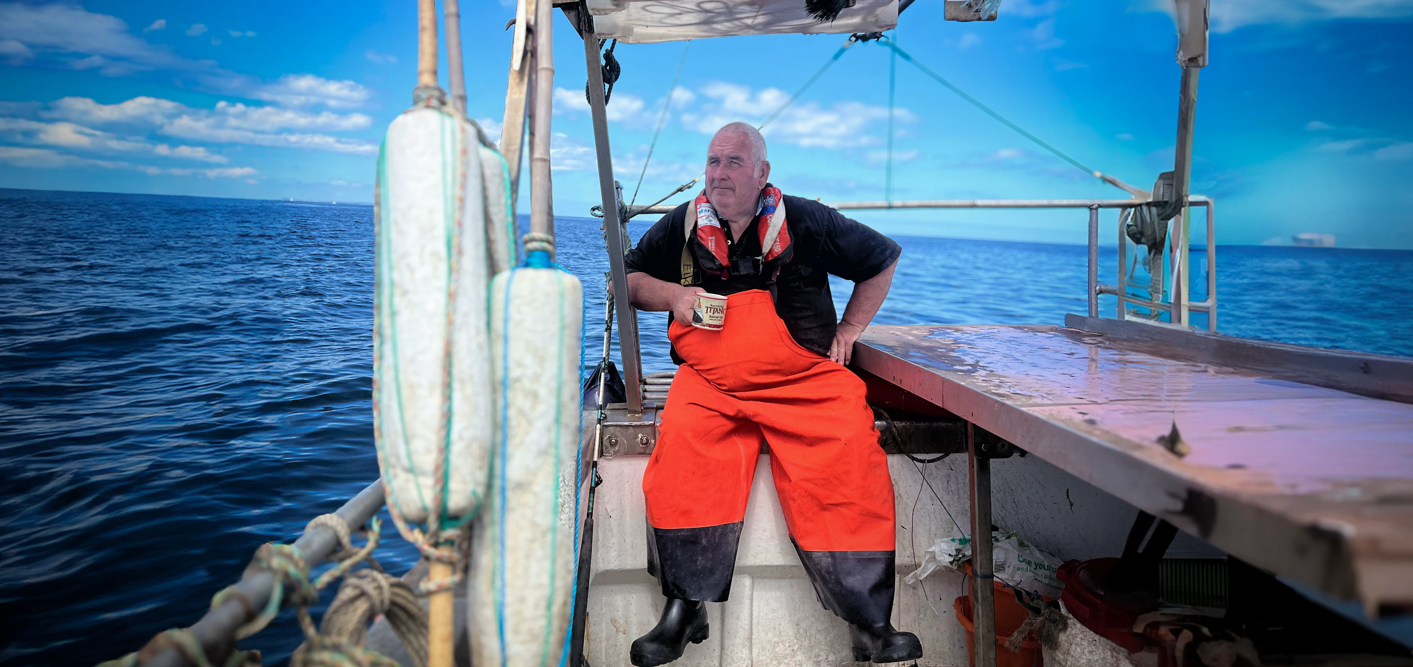 Fisherman in red overalls on a boat against blue sky