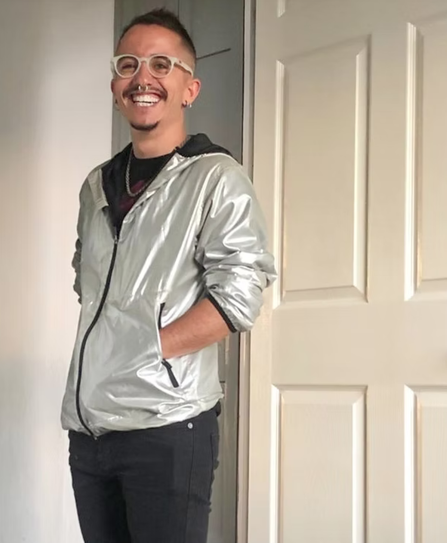 a man in a silver jacket smiles and looks to camera