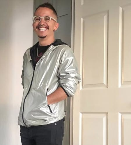 a man in a silver jacket smiles and looks to camera