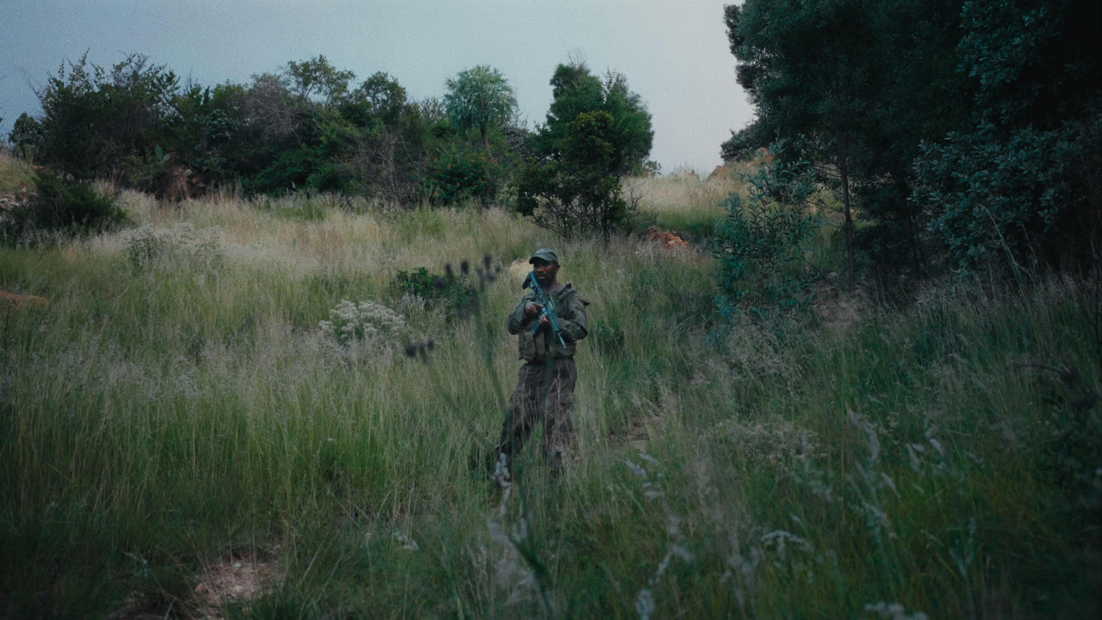 a man in camouflage gear with a gun in the countryside