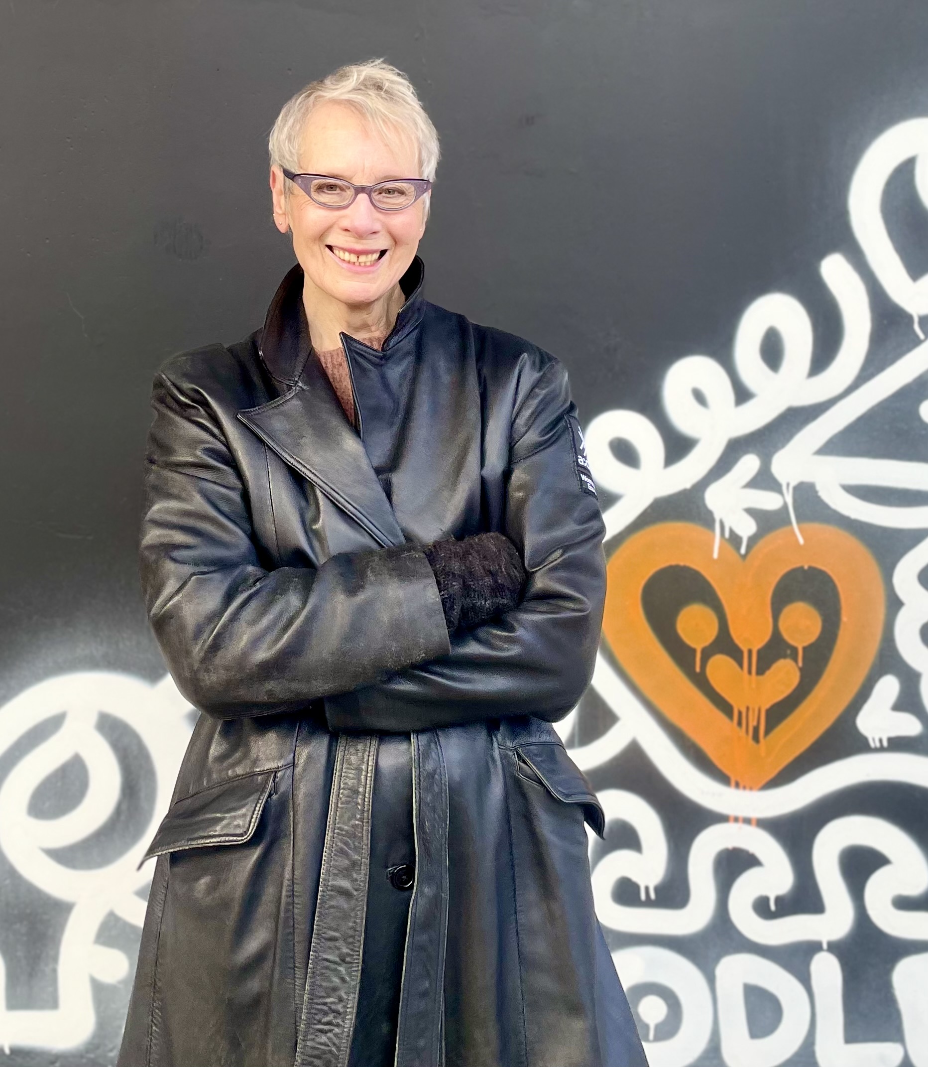 A woman in leather coat stands against a graffiti background