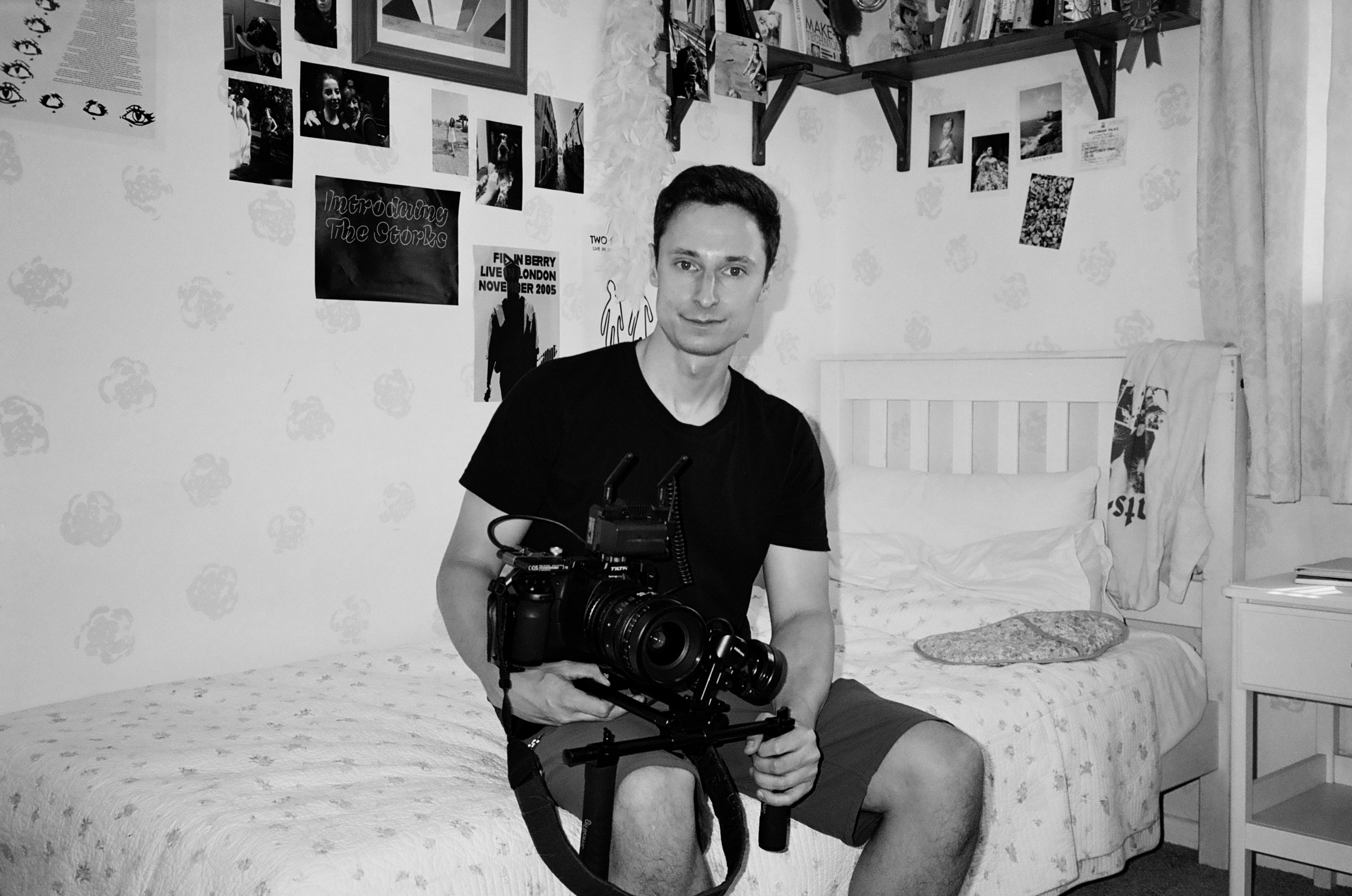 A man with camera sits in his bedroom