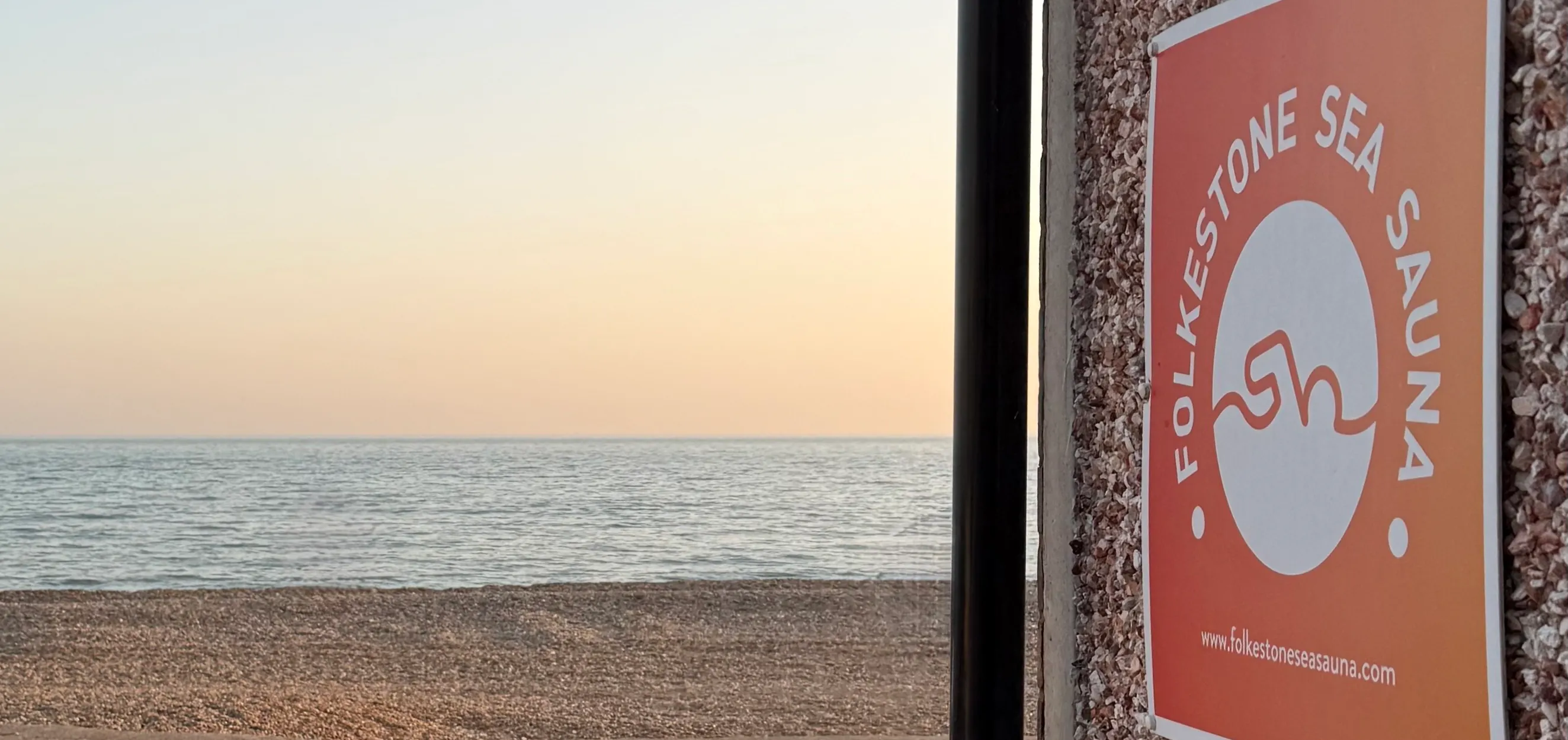 View over the sea at Sandgate with the Folkestone Sea Sauna sign in the foreground