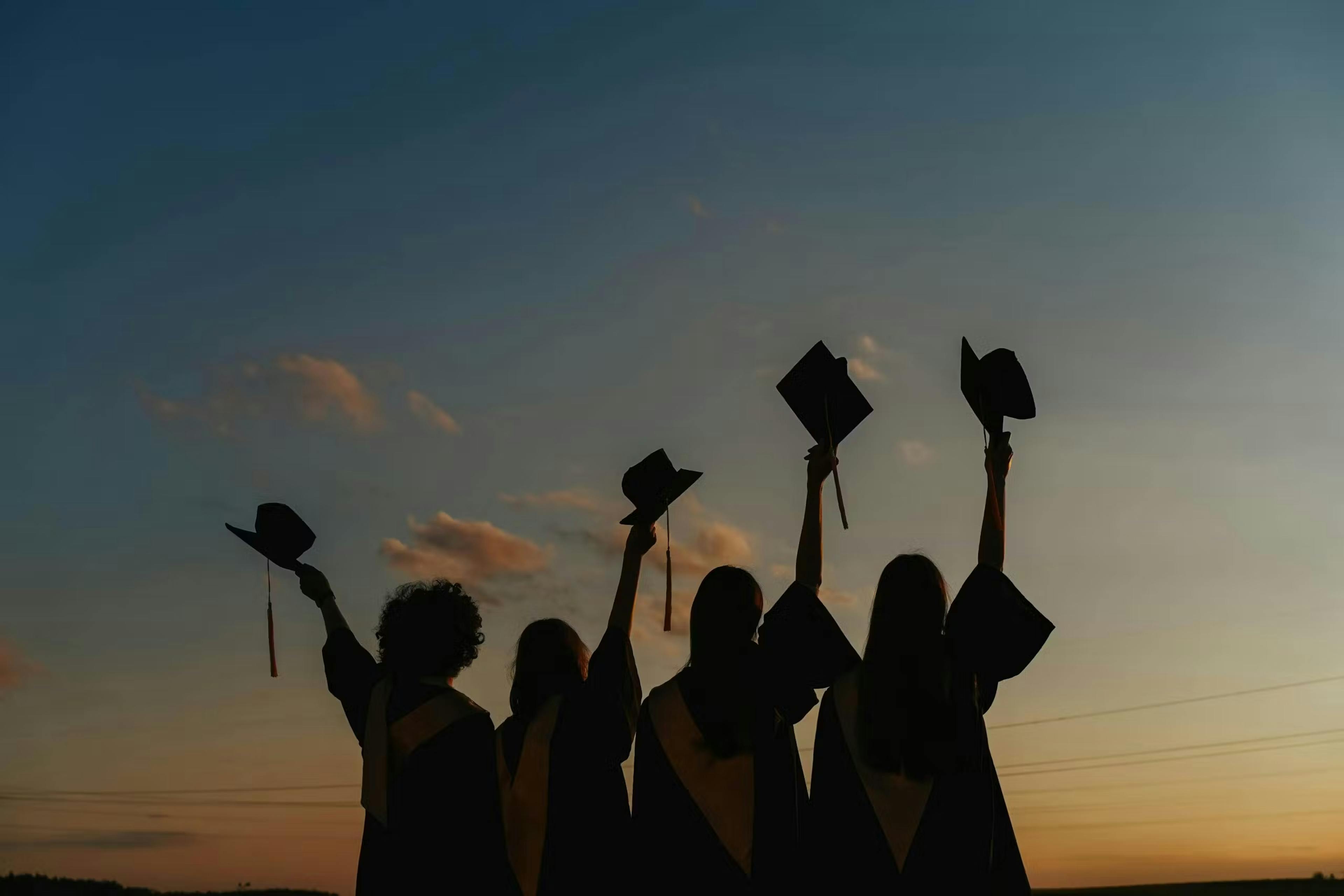 Ragazze alzano al cielo i cappelli della laurea al tramonto