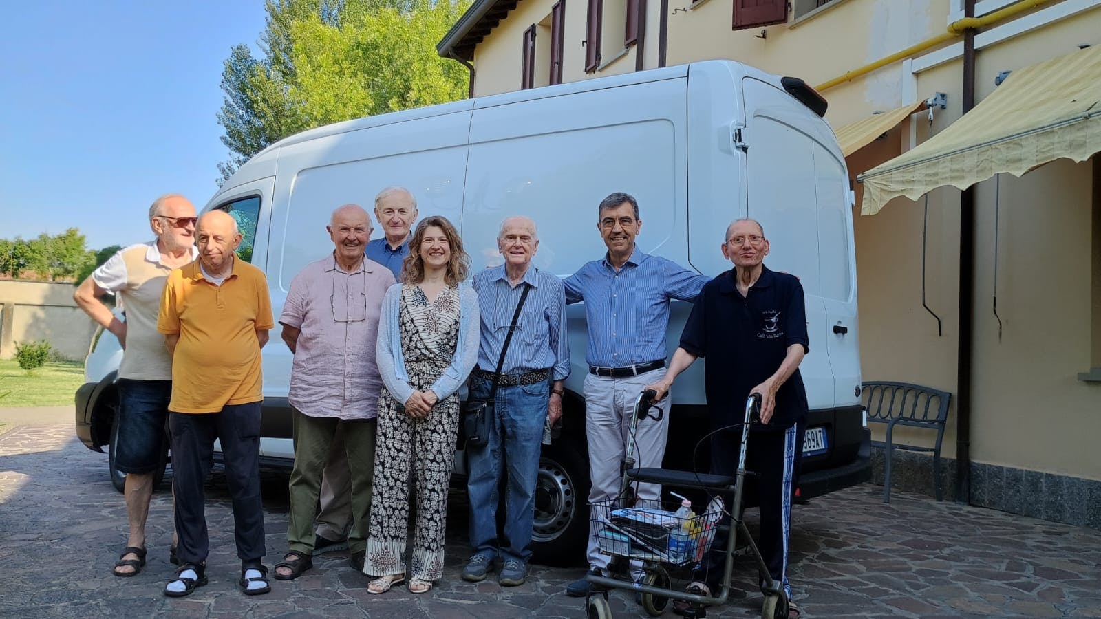 Gruppo per lo più di uomini anziani in piedi davanti a furgone bianco davanti a edificio in una giornata di sole