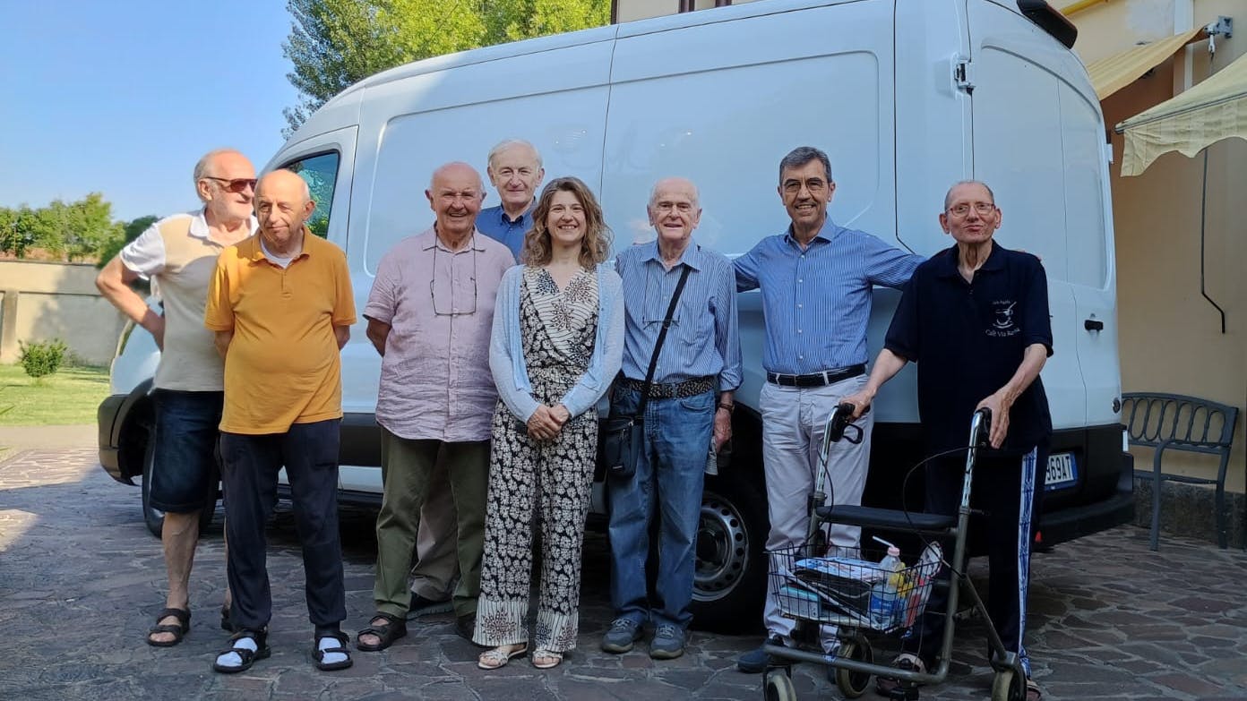 Gruppo per lo più di uomini anziani in piedi davanti a furgone bianco davanti a edificio in una giornata di sole