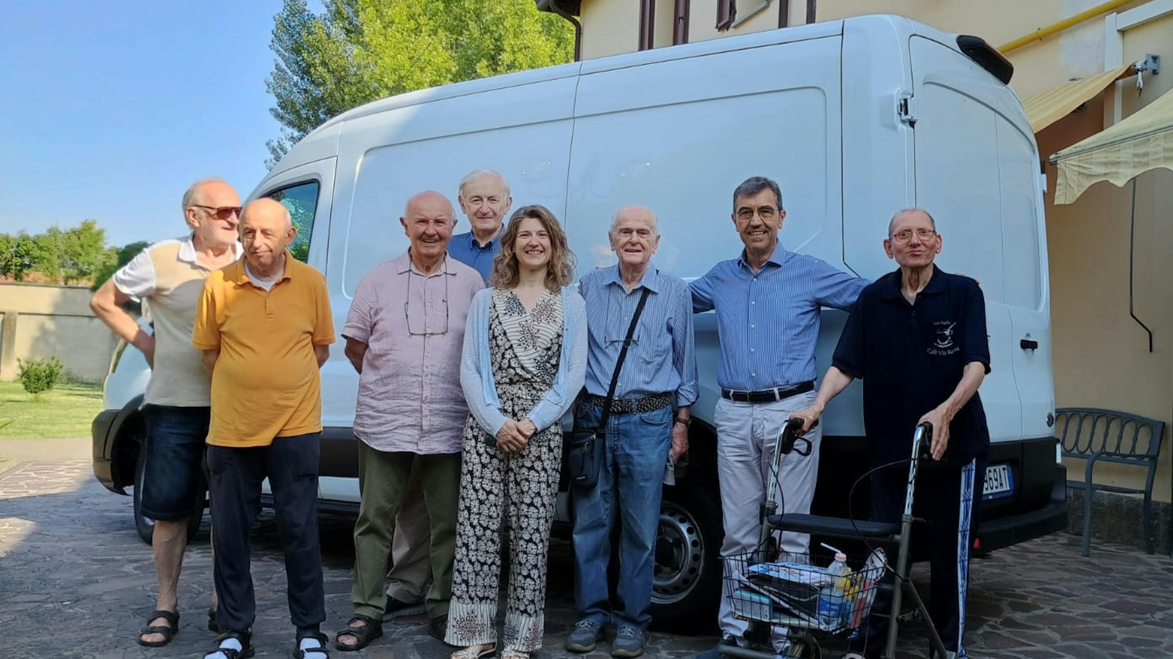 Gruppo per lo più di uomini anziani in piedi davanti a furgone bianco davanti a edificio in una giornata di sole