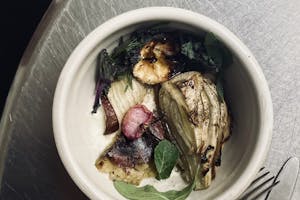 Photo of a meal of grilled avocado and vegetables with silverware on a silver table