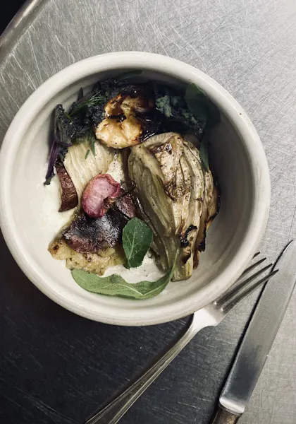 Photo of a meal of grilled avocado and vegetables with silverware on a silver table