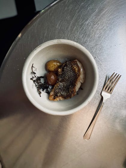 Photo of a bowl of grilled fish and a fork on a silver table