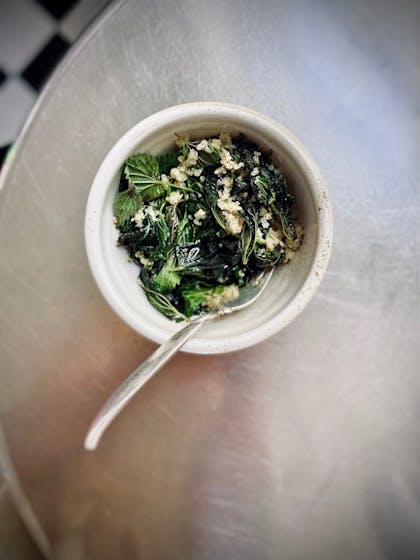 Photo of a bowl of salad with dark leafy greens and a fork on a silver table