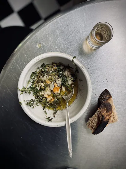 Photo of a bowl of salad with bread and drink on a silver table