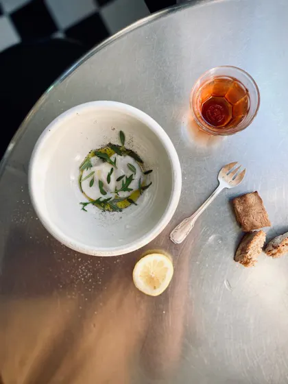 Photo of poached eggs, a spork, half a squeezed lemon, bread ends and a reddish drink on a silver table.