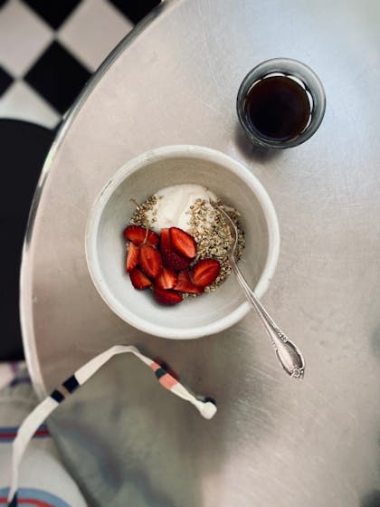 Photo of a bowl of yoghurt with strawberries and a drink on a silver table.