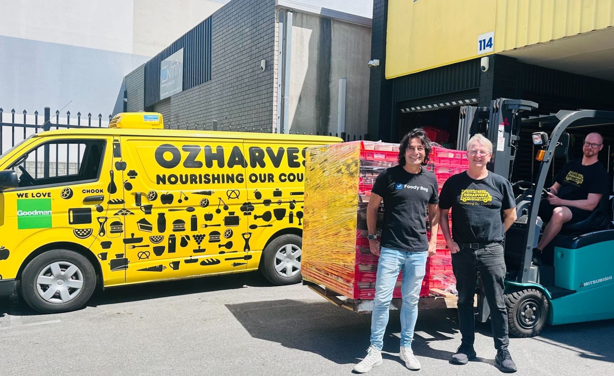 A yellow OzHarvest van beside a pallet of crates being loaded by forklift