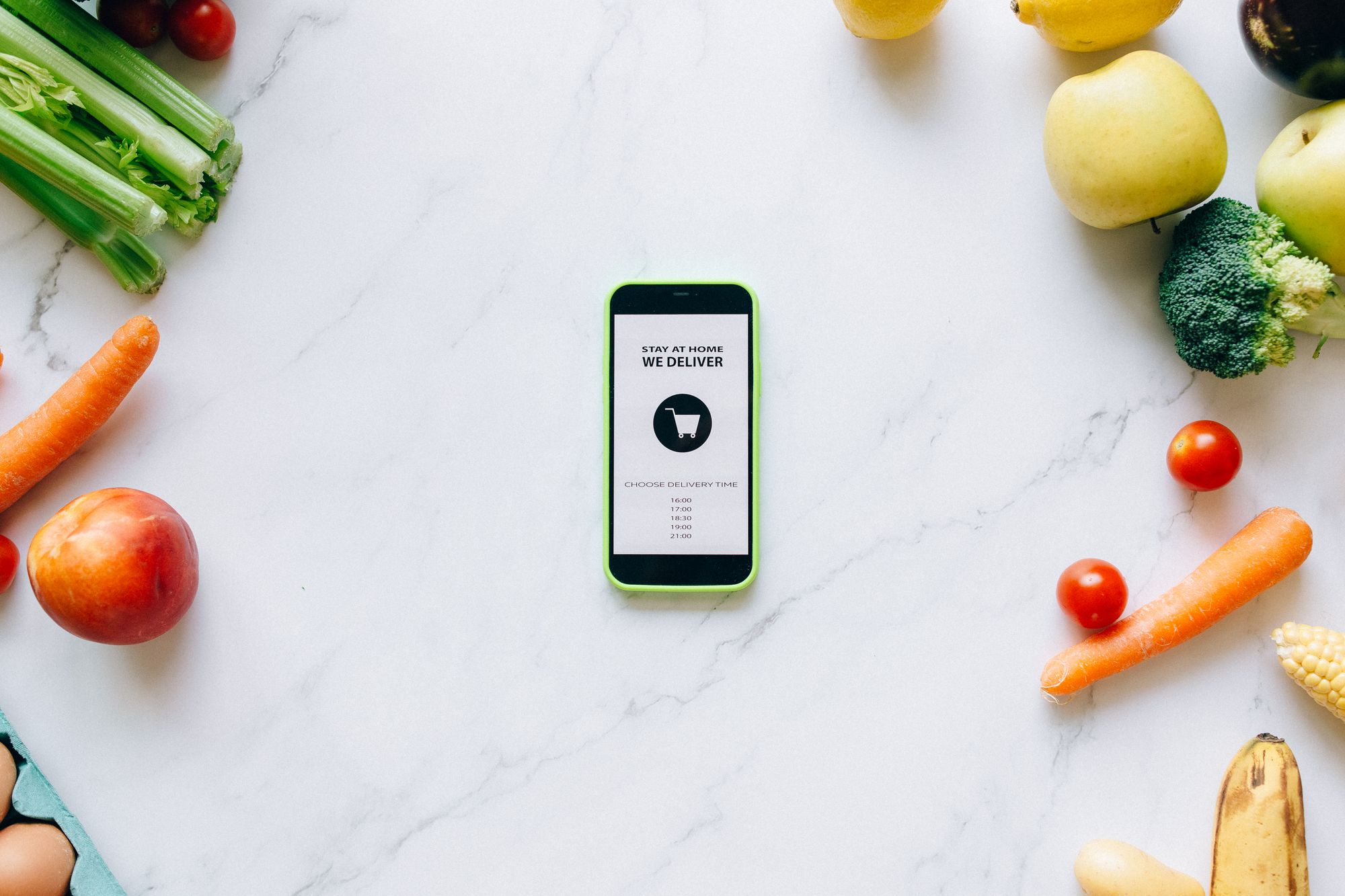 A phone on a kitchen counter surrounded by fruit and vegetables